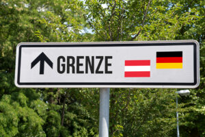 Straßenschild mit Pfeil nach oben, Aufschrift „GRENZE" sowie den Flaggen Österreichs und Deutschlands