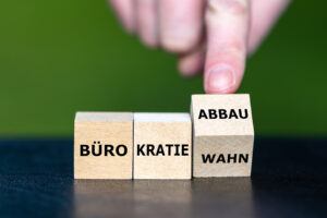Eine Hand dreht einen Holzwürfel, sodass aus „Bürokratiewahn" der Begriff „Bürokratieabbau" wird