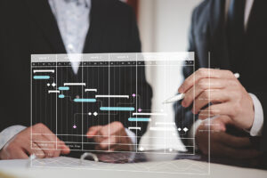 Zwei Personen im Anzug betrachten ein digitales Gantt-Diagramm mit Projektphasen über sechs Wochen