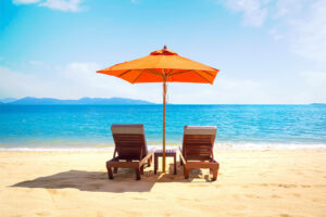 Zwei Liegestühle mit orangefarbenem Sonnenschirm an einem sonnigen Sandstrand mit türkisblauem Meer